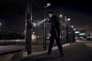 Security guard inspecting perimeter fence at night